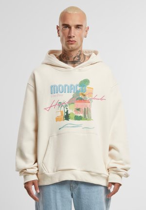 Cream-colored hoodie featuring a graphic print of a tropical scene with "Monaco" and "Côte d'Azur" text, textured fabric, and front pocket.
