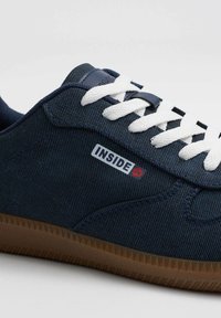 Zapatilla de lona azul marino con cordones blancos, suela de goma y una superficie texturizada. Presenta un logo "INSIDE" en rojo y blanco.