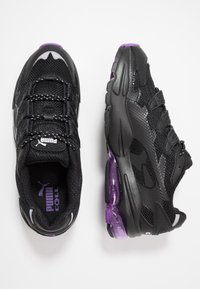 Svarta sportskor med en texturerad mesh-övre del, med snören, lila detaljer och en genomskinlig lila häldel.