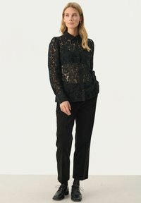 Zwarte kanten blouse met een kraagontwerp, lange mouwen en knoopsluiting. Gecombineerd met zwarte corduroy broek en zwarte schoenen.