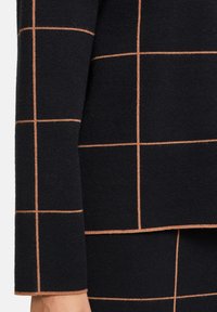 Marineblausestricktop mit einem Karomuster in hellbraunen Linien, das einen strukturierten Stoff und ein leicht ausgestelltes Ärmeldesign präsentiert.