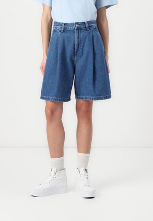 Denimshorts i en lys blå vask, med høy midje, plisserte detaljer foran og løs passform. Kombinert med hvite høye sneakers og ribbestrikkede sokker.