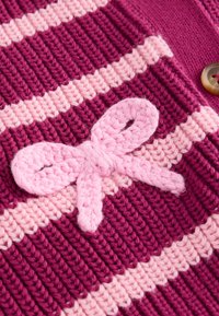 Tissu tricoté présentant des rayures horizontales alternées magenta foncé et rose clair, avec un détail de nœud tricoté rose clair sur la surface.