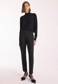 Czarny, długi rękaw, golfowy top zestawiony z dopasowanymi, wysokimi spodniami w kolorze czarnym. Modelka nosi czarne szpilki w szpic z kwiatowymi akcentami.