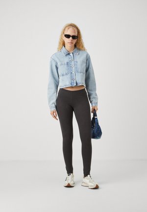 Lys blå, avskåret denimjakke, svarte leggings og hvite sneakers, holder en blå håndveske. Solbriller fullfører antrekket.