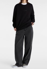 Černá mikina s vyraženým logem „vans.“, doplněná volnými tmavě šedými kalhotami a černobílými kostkovanými slip-on botami.