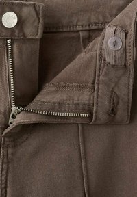 Țesătură maro din bumbac cu închidere cu fermoar, nasture metalic și margini cusute. Căptușeala interioară este netedă și se potrivește cu culoarea exterioară.