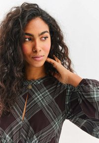 Czarna i zielona koszula w kratę z wycięciem typu keyhole, długimi bufiastymi rękawami i miękką fakturą, ozdobiona delikatnym złotym naszyjnikiem.