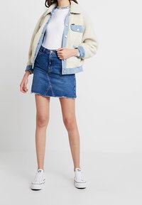 Giacca in denim e pelliccia sintetica di colore crema e azzurro chiaro, abbinata a una maglietta bianca attillata e una minigonna in denim azzurro chiaro. Sneakers bianche.