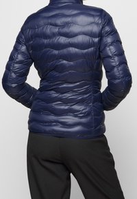 Navy blue padded jacket with a high collar and wavy quilted texture, featuring a fitted design and smooth, shiny fabric.