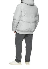 Grijze pufferjack met een capuchon, voorzien van een gewatteerd ontwerp en elastische manchetten. Gekocht met donkergrijze broeken en witte sneakers.