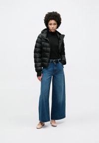 Μαύρο καπιτονέ μπουφάν με κουκούλα, μαύρο μακρυμάνικο τοπ, μπλε τζιν παντελόνι με φαρδιά μπατζάκια και ανοιχτόχρωμα παπούτσια. Λείο ύφασμα και μοντέρνα εφαρμογή.