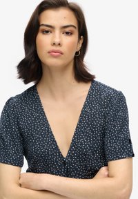 Granatowa sukienka z krótkimi rękawami i głębokim dekoltem w kształcie litery V. Posiada mały biały wzór kwiatowy oraz guziki z przodu. Gładka tekstura materiału.