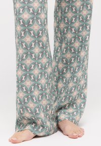 Lässige Stoffhose mit einem sich wiederholenden geometrischen Muster in Grün, Grau und Creme, versehen mit subtilen gelben Akzenten und einer weichen Textur.