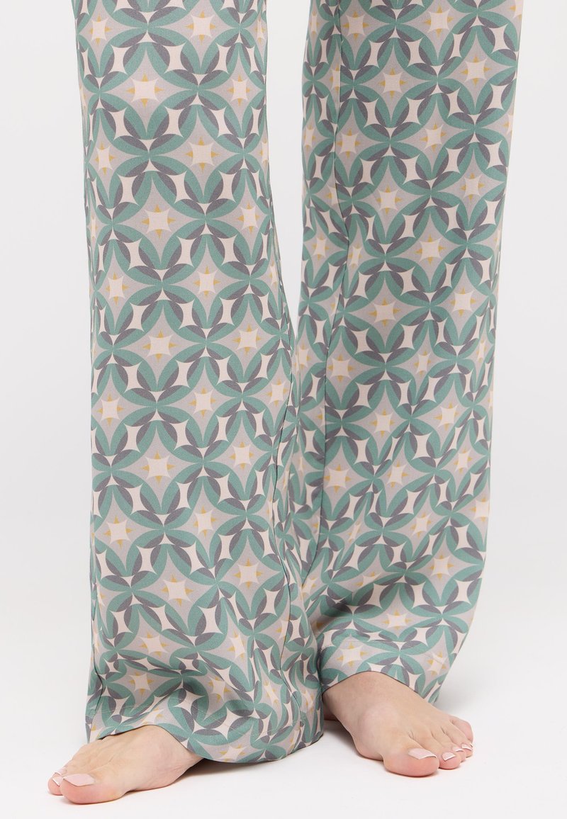 Lässige Stoffhose mit einem sich wiederholenden geometrischen Muster in Grün, Grau und Creme, versehen mit subtilen gelben Akzenten und einer weichen Textur.