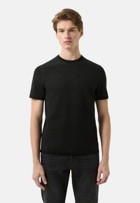 Sort t-shirt med korte ærmer lavet af blødt stof, med rund hals og glat tekstur, kombineret med mørke jeans.