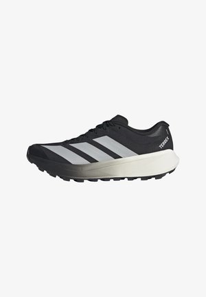 Černobílá trailová běžecká bota Adidas Terrex s tlustou podrážkou a třemi reflexními pruhy na boku na bílém pozadí.