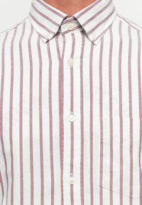Collared white shirt with vertical red and navy stripes, buttoned up, featuring a chest pocket on the right side.