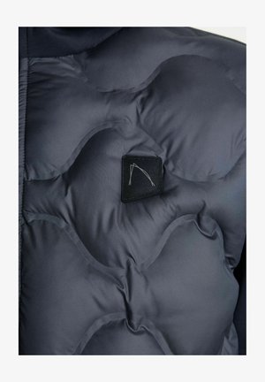 Nahaufnahme einer dunkelblauen Steppjacke, die ihre gesteppten Texturen und ein kleines schwarzes Logo-Patch im Brustbereich zeigt.