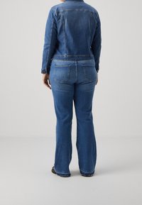 Veste en denim à manches longues et fermetures à boutons, associée à un jean bleu évasé avec poches arrière et un détail d'ourlet brut.