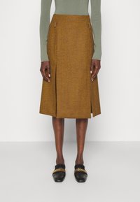 Brun herringbonekjol med knä-lång längd, som har sidofickor och en mittsids slit. Kombinerad med svarta tofflor med guldchain-accenter.