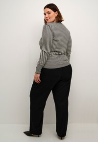Zwart-wit gestreepte blouse met lange mouwen gecombineerd met losse zwarte broeken. De outfit heeft een gestructureerde afwerking en aangesloten manchetten.