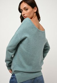 Himmelblaues, weiches Strickpullover mit einem Off-Shoulder-Design und langen Ärmeln. Hat eine entspannte Passform sowie einen gerippten Saum und Bündchen.