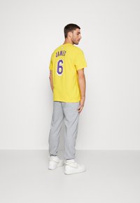 Tricou galben din bumbac cu "JAMES" și numărul "6" în violet pe spate. Purtați cu pantaloni de trening gri și adidași înalți albi.