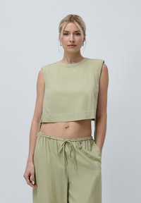 Lichtgroene cropped top met een ronde hals en korte mouwen, gemaakt van gladde stof. In combinatie met bijpassende lichtgroene joggingsbroek met trekkoord.