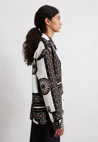 Camicia a righe bianche e nere con design circolari e forme geometriche, con colletto classico e maniche lunghe.