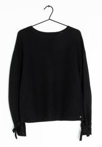 Schwarzer, langärmliger Strickpullover mit Rundhalsausschnitt und gebundenen Schleifen an den Ärmelbündchen, die an einem schwarzen Drahtbügel vor einem weißen Hintergrund hängen.