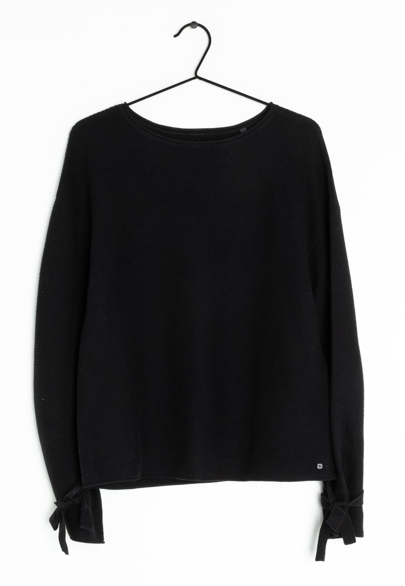 Schwarzer, langärmliger Strickpullover mit Rundhalsausschnitt und gebundenen Schleifen an den Ärmelbündchen, die an einem schwarzen Drahtbügel vor einem weißen Hintergrund hängen.