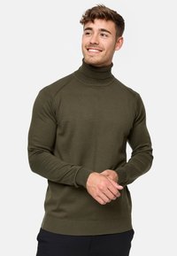 Maglione a collo alto color verde oliva realizzato in un materiale a maglia a coste. Caratterizzato da maniche lunghe, una silhouette aderente e un orlo ampio.