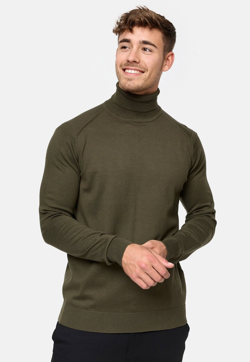 Maglione a collo alto color verde oliva realizzato in un materiale a maglia a coste. Caratterizzato da maniche lunghe, una silhouette aderente e un orlo ampio.