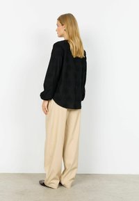 Musta pusero, jossa on teksturoitu kukkakuosi, pitkät hihat, rento istuvuus; yhdistetty beigen värisiin leveälahkeisiin housuihin ja tummiin matalavartisiin kenkiin.