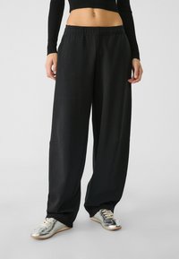 Zwarte wijde broek van zachte stof, met een elastische tailleband en twee zijzakken, gecombineerd met zilveren sportchoenen.