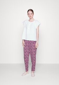 Top branco de manga curta com detalhes em botão, combinado com calças padrão cor-de-rosa e sapatos slip-on de cor clara. Tecido suave e leve.