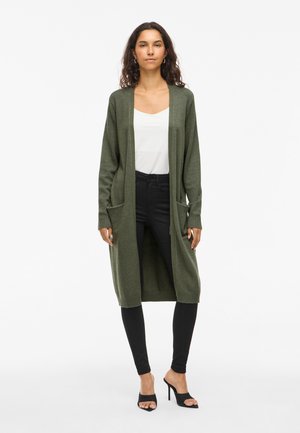 Long olive green cardigan with two front pockets, open front and ribbed cuffs, worn over a white top and black skinny pants.