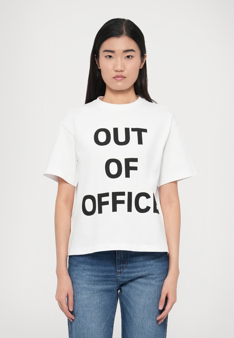 Λευκό βαμβακερό μπλουζάκι με άνετη γραμμή, με έντονα μαύρα γράμματα "OUT OF OFFICE" τυπωμένα στο μπροστινό μέρος. Κοντά μανίκια και στρογγυλή λαιμόκοψη.