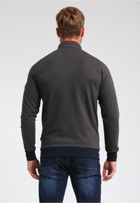 Maglione grigio scuro con una texture, colletto alto e polsini a coste blu navy, abbinato a jeans blu, visto da dietro.