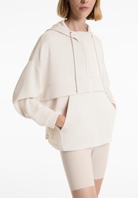 Un hoodie surdimensionné de couleur crème en tissu doux avec une poche kangourou, un capuchon à cordon de serrage et des poignets côtelés, associé à un short de vélo assorti.