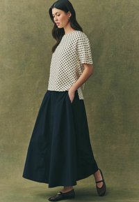Cremefarvet top med polkaprikker og korte ærmer, parret med en gulvlang marineblå skirt, der har en glat tekstur og en A-formet silhuet.