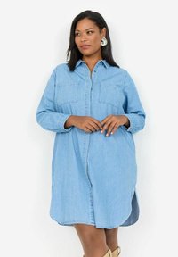 Gaišas zila džinsu krekla kleita ar garām piedurknēm, pogu aizdari, divām krūškurvja kabatām un sānu šķēlumiem, kas nodrošina brīvu kustību.