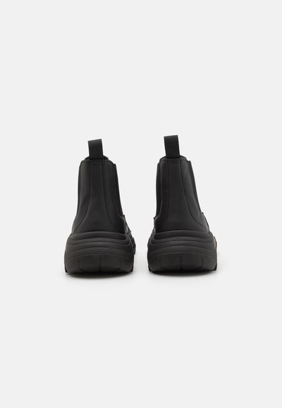 Svarta höga sneakers med en strukturerad ovandel, elastiska sidopaneler och tjocka gummisålar. Utrustade med dragflikar på baksidan för enkelt på- och avtagande.