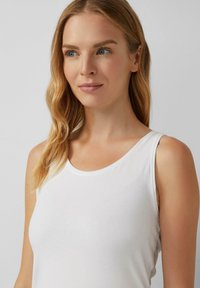 Witte tanktop van een gladde, rekbare stof. Heeft een ronde halslijn, brede schouderbanden en een aansluitende snit.