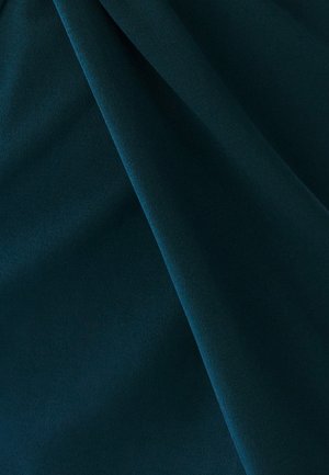 Temno zeleni tekstil z gladko teksturo, ki vsebuje nežen drapež, ki ustvarja globino in dimenzijo. Oblika poudarja mehak drapež.