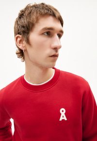 Rode sweatshirt van een katoenmengsel, met een ronde hals, ribgebreide boorden en een witte logo op de borst. Gladde textuur, casual ontwerp.
