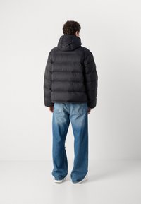 Schwarze Puffjacke mit Kapuze, ausgestattet mit einem gesteppten Design und einem leicht verkürzten Schnitt, getragen über hellblauen, weiten Jeans.