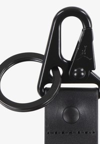 Black metal keychain clip with a circular ring attachment, featuring a textured black strap and a small logo detail on the clip.