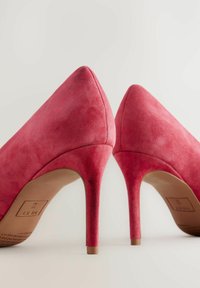 Tacchi alti in suede rosa con punta affilata e sottile tacco a stiletto. Texture morbida e finitura liscia, con suola beige e logo del brand.